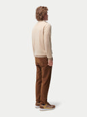 Person wearing a beige sweater and brown pants on a white background