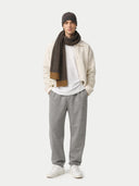 Person wearing a beige jacket, white shirt, gray pants, and a brown scarf on a white background #color_charcoal