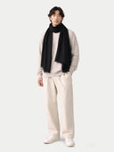 Man wearing a black scarf, light gray sweater, white pants, and white shoes on a white background