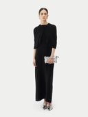 Front view of a black short-length capelet over a black dress and holding a silver handbag on a light gray background #color_black