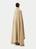 back view of a person wrapped in a beige cable knit blanket with a subtle pattern. #color_beige