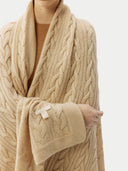 close up of a person wrapped in a beige cable knit blanket with a subtle pattern. #color_beige