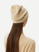 close up back view of a woman wearing a beige beanie hat matching sweater on a light gray background #color_beige