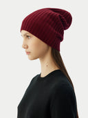 side view of a woman wearing a maroon beanie and a black sweater.