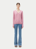 front view of a woman wearing a pink v-neck sweater and blue jeans.