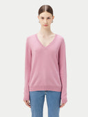 A woman wearing a pink V-neck cashmere sweater with long sleeves, paired with blue jeans.