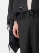 close up of a dark gray fringed blanket with a black brand label "GOBI" and black pants #color_charcoal