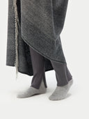 close up bottom side view of a person wearing a gray blanket with fringes, dark pants, and gray socks on a white background #color_charcoal