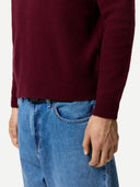 Close up of a maroon sleeve of sweater detail and blue jeans on a white background #color_zinfandel