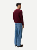Back view of a person wearing a burgundy sweater and blue jeans on a white background #color_zinfandel