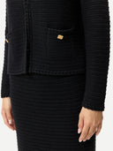 Close up of a black textured suit cardigan with gold buttons and matching knit cashmere skirt on a plain background #color_black