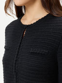 Close-up of a person wearing a black textured crew neck cardigan with side pocket lines on the chest on a white background #color_black