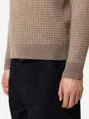 Close-up of a person wearing a brown textured sweater and black pants on a white background #color_taupe
