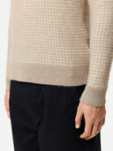 Close up of a beige textured sweater worn by a person on a white background #color_warm-grey