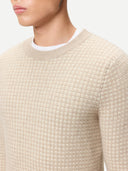 Close-up of a person wearing a textured beige crew-neck sweater with a white collar. #color_warm-grey