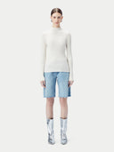 Person wearing a white turtleneck sweater, light blue shorts, and silver rain boots on a white background #color_whisper-white
