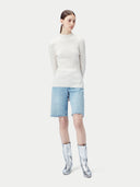 Person wearing a white sweater, light blue shorts, and silver boots on a white background #color_whisper-white