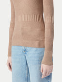A close-up side view of a person wearing a camel-colored, ribbed sweater with a lined pattern of varying rib widths, and  blue jeans, set against a light gray background. #color_timber-wolf