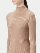 A close-up side view of a person wearing a camel-colored, ribbed turtleneck sweater with a geometric pattern of varying rib widths, set against a light gray background. #color_timber-wolf
