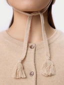 Close-up of a beige knitted cardigan with tassel details on a plain background #color_beige