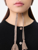 Close-up of a person wearing a black sweater with a brown knitted hat featuring tassels. #color_taupe