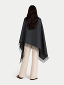 back view of a person wrapping a dark gray blanket with fringe details on a white background #color_charcoal