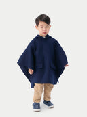 A child wearing a navy hooded cashmere poncho with a plain background. #color_navy