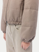 A close-up shot of the lower half of a taupe, quilted puffer jacket with an elasticized hem and cuffs, paired with light olive-colored trousers. #color_taupe