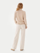 back view of a woman wearing a beige sweater and white pants on a white background #color_beige