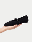 Black flat shoe with a strap held by a hand on a white background #color_black