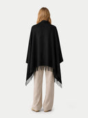 back view of a woman wrapped a black blanket with fringe details on a white background.