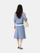 Woman wearing a blue outfit with a white bag on a light gray background #color_dusty-blue