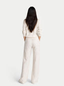 back view of a person wearing a white outfit with wide-leg pants on a light gray background #color_off-white