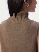Close-up back view of a person wearing a ribbed knit sleeveless turtleneck sweater in taupe brown, with a small silver hoop earring visible against a light gray background.