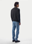 A man shown from the back wearing a dark charcoal gray knit sweater, light blue jeans, and black shoes, standing against a plain light gray studio background.