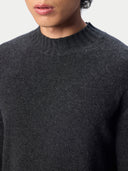 Close-up of a person wearing a dark charcoal gray knit sweater with a ribbed crew neck, against a light gray background.