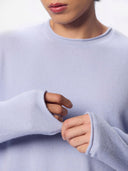 A close-up of a man wearing a light blue knit sweater, showing the rolled-edge neckline and cuff.