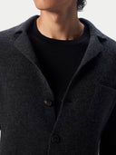 Close-up of a person wearing a dark charcoal gray wool-blend jacket over a black crewneck shirt, against a light gray background.