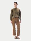 A model stands against a light gray studio background wearing a fuzzy olive green mock-neck sweater, brown cropped trousers, and brown suede loafers.
