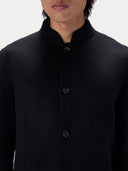 Close-up of a person wearing a black long-sleeve jacket with a mandarin collar and dark buttons, against a plain light background.