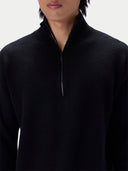 A close-up of a person wearing a black quarter-zip knit sweater against a light gray studio background.