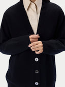A close-up of a person wearing a black knit cardigan over a light beige collared shirt, with the cardigan buttons visible against a plain light background.