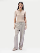 A model stands against a light gray studio background wearing a beige ribbed short-sleeve polo shirt with thin red and blue stripe accents at the collar and sleeve cuffs, paired with light beige wide-leg trousers and beige shoes.