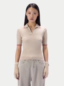 A model wearing a beige ribbed short-sleeve polo shirt with thin red and white striped accents on the collar and sleeve cuffs, paired with light gray pants and matching beige knit fingerless gloves, against a solid light gray background.