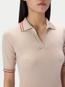 A close-up of a woman wearing a beige ribbed short-sleeve polo shirt with red stripe accents on the collar and sleeve cuffs, set against a plain light background.