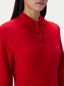 A close-up of a model wearing a bright red knit polo sweater with three dark buttons, set against a plain light gray background.