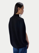A woman shown from the back wearing a black mock-neck knit top and blue jeans against a light gray studio background.