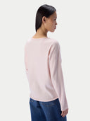 A woman shown from the back wearing a light pink long-sleeve knit top and blue jeans against a plain light gray studio background.