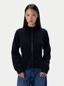 A woman modeling a black long-sleeve mock neck knit cardigan with a button-down front, paired with blue jeans, against a light gray studio background.