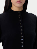 Close-up of a person wearing a black knit top with a high mock neck and a vertical row of dark buttons down the front, against a light gray background.